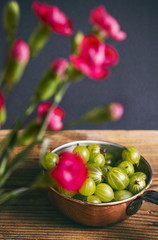 Gooseberries in a copper pot with fresh pink carnations in the foreground