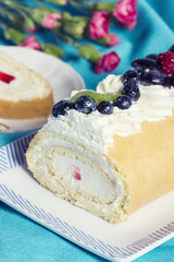 Homemade cream roll cake decorated with fruits on ceramic plate