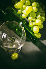 Wine glass, green bottle and bunch of white grapes on dark background