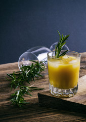 Orange alcoholic drink with rosemary and ice on wooden board