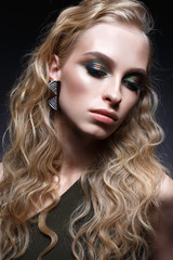 Young girl with curls and bright creative make-up. Beautiful model in earrings and green top. Beauty of the face. Photo is taken in the studio. evening image.
