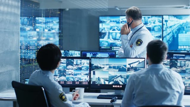 In the Security Control Room Chief Surveillance Officer Holds a Briefing for Two of His Subordinates. Multiple Screens Show that They Guard Object of Big Importance. 