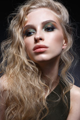Naklejka premium Young girl with curls and bright creative make-up. Beautiful model in earrings and green top. Beauty of the face. Photo is taken in the studio. evening image.