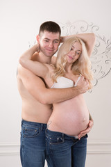 Beautiful pregnant couple in love on the background. Hands of husband on the tummy of his pregnant wife. Young man tenderly stroked pregnant belly of his wife. Husband kissing pregnant belly.