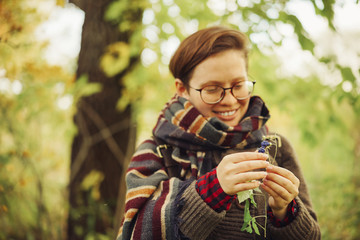 cute happy girl in glasses with a sweatshirt and a scarf found in the forest blueberries and wants to eat it. autumn forest berries and people. focus on blueberries in hands.