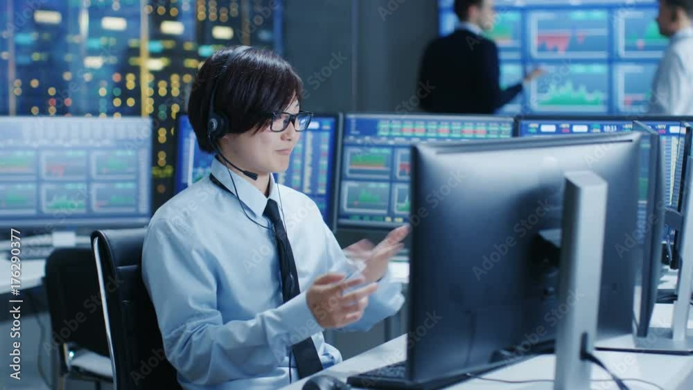 Poster In the Network Operations Center Trader Makes Personal Client Call with a Headset. In the Background Traders Discuss Data Shown on Monitors. Shot on RED EPIC-W 8K Helium Cinema Camera.