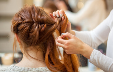 Fototapeta premium Beautiful, red-haired girl with long hair, hairdresser weaves a French braid, in a beauty salon. Professional hair care and creating hairstyles.
