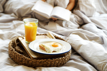 Simple breakfast in bed. Fried eggs with orange juice on tray. Girl with book in the background 

