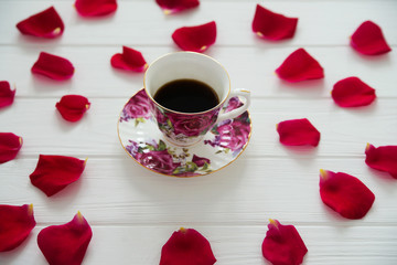 Cup of coffee in red roses petals on the white background