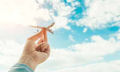 hand holding airplane model in front of cloudy blue sky background. air transportation concept.