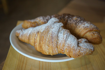 two croissants on a plate, sprinkled with powdered sugar