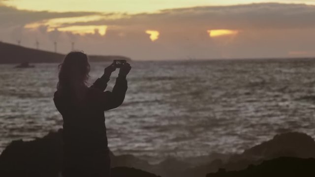 A girl makes a sea sunset photo using a mobile device