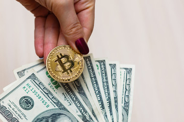 Golden bitcoin coin on women's hand on blurred us dollar bills background copy space