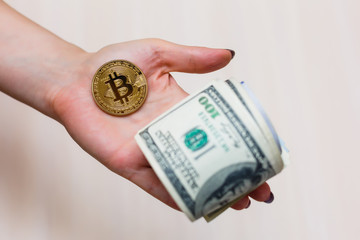 Golden bitcoin coin on women's hand on blurred us dollar bills background copy space