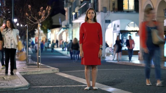 Timelapse of woman standing still on crowded evening street while a blur of fast moving people move around her