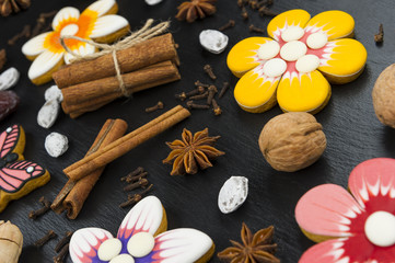 Gingerbread cookies with nuts and spices, colorful homemade cakes in shape of flower on black textured background, selective focus 