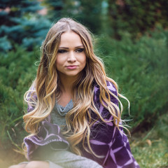 Fototapeta premium Gorgeous girl wrapped in a coverlet sits on the grass