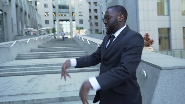 Afro-American male in business suit making funny dance movement near office