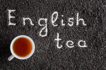 Inscription English tea created on black, dried, loose tea with cup. Enjoying of tea break at the work, at home, at visit with friends, family or alone everyday. Classic warm or hot drink. Top view.