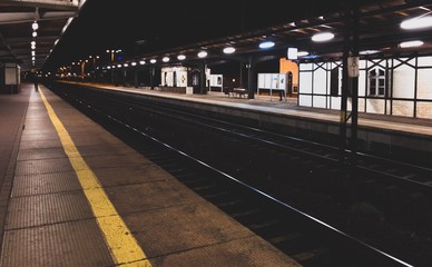 widok na dworzec kolejowy w nocy, żółta linia bezpieczeństwa na peronie i oświetlony dalszy...