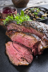Barbecue haunch of venison with mushrooms and cranberry Sauce as close-up on a slate slab