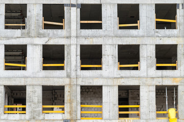 Betonfassade eines Hochhauses mit leeren Fensteröffnungen und gelben Holzbalken 