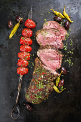Barbecue lamb roast with skewered tomatoes and olives as close-up on a board