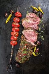 Gardinen Barbecue lamb roast with skewered tomatoes and olives as close-up on a board © HLPhoto