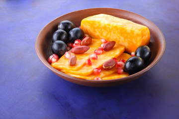 Orange cheese, sliced cheese, a sort of hard cheese, marbled cheese, dark blue grapes, peanuts and pomegranate seeds in a clay plate on a dark blue background