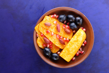 Orange cheese, sliced cheese, a sort of hard cheese, marbled cheese, dark blue grapes, peanuts and pomegranate seeds in a clay plate on a dark blue background