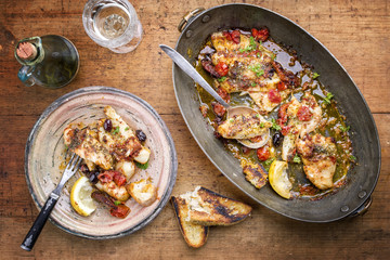 Fried John Dory fish fillet with vegetable and baguette as top-view in a casserole .