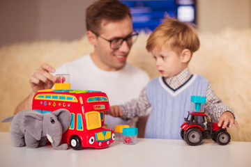 Portrait of young happy father and little cute son who playing with toys indoors