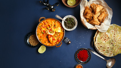 Indian cuisine on diwali holiday: tikka masala, samosa, patties and sweets with mint chutney and spices. Dark blue background. Banner composition with copy space