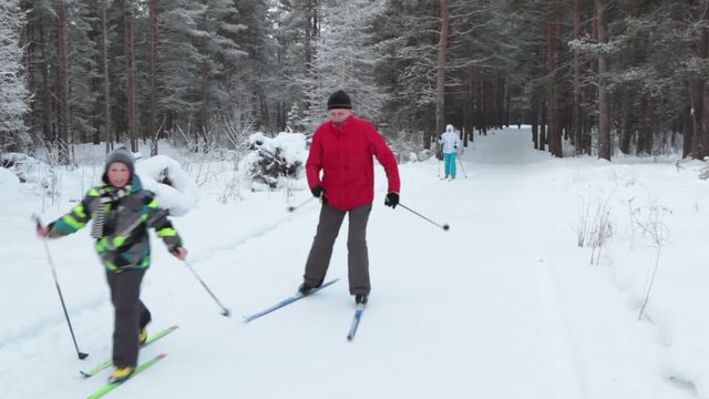 Family with senior father, son and young mother skiing in winter forest together