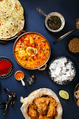 Indian cuisine on diwali holiday: tikka masala, samosa, patties and sweets with mint chutney and spices. Dark blue background. Vertical composition