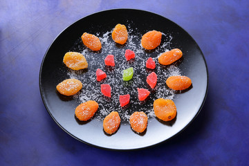 Dried apricots, candied fruits in sugar on a black plate on a dark blue background in retro style
