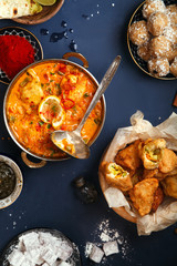 Indian cuisine on diwali holiday: tikka masala, samosa, patties and sweets with mint chutney and spices. Dark blue background, top view.