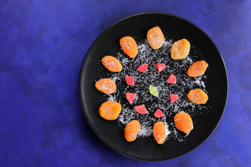 Dried apricots, candied fruits in sugar on a black plate on a dark blue background in retro style