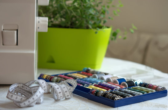 Sewing tools on the table - a set of multi-colored threads on bobbins, roulette seamstresses and part of the sewing machine