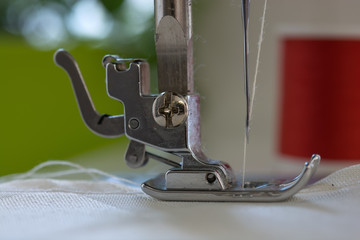 The sewing machine's foot with a needle sews ecru color  fabric. Close -up
