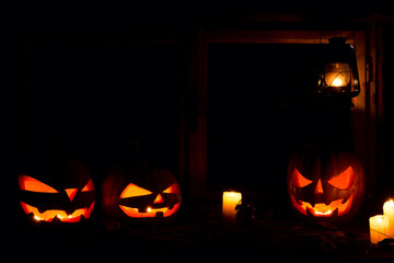 Halloween - pumpkins, candles and a lamp on leaves and logs, against the background of a window