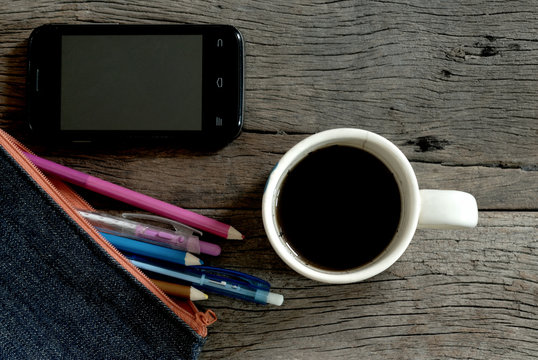 cup of coffee on wooden table with smart phone and pen in fabric bag