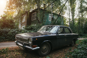 Aged vintage soviet black retro car on background of green wooden old house