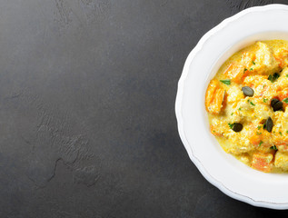 Baked pumpkin with chicken and cream sauce in a white plate on a dark stone background, top view