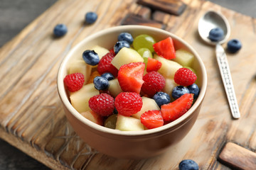 Bowl with yummy fruit salad on wooden board