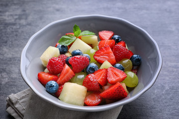 Bowl with yummy fruit salad on grunge table