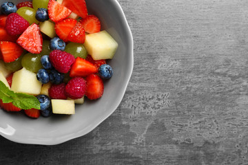 Bowl with yummy fruit salad on grunge table