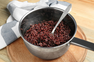 Cooked rice in saucepan on wooden board