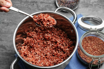 Woman holding spoon with cooked rice over saucepan
