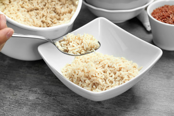 Woman pouring cooked rice from saucepan to plate on table